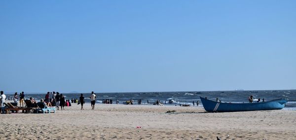 People at beach against clear blue sky