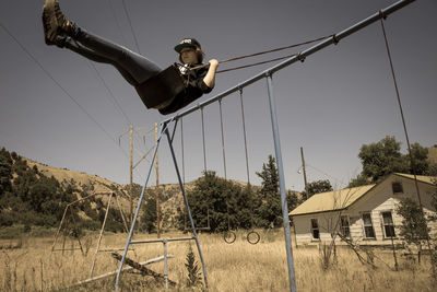 Low angle view of woman enjoying swing on grassy field against sky