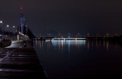 Illuminated city by river against clear sky at night