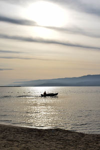 Silhouette people in sea against sky during sunset