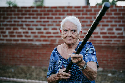 Senior woman holding stick against brick wall
