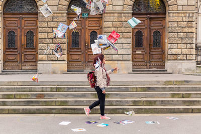 Side view of woman walking amidst falling printed media against building