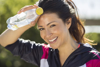 Portrait of happy fit woman wiping sweat while holding water bottle