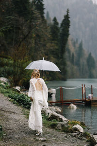 Beautiful young woman bride in a boho dress and with an umbrella stands in the rain in nature