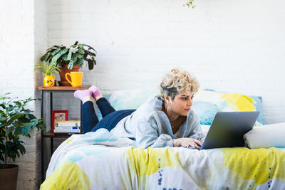 Mid adult woman using laptop while lying on bed in bedroom at home