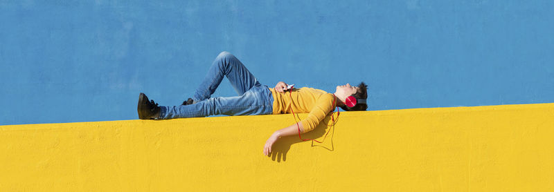 Side view of young woman lying on yellow wall