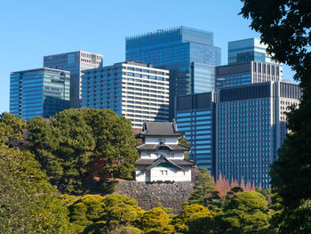 Japanese castle guard tower and modern buildings in city against clear sky