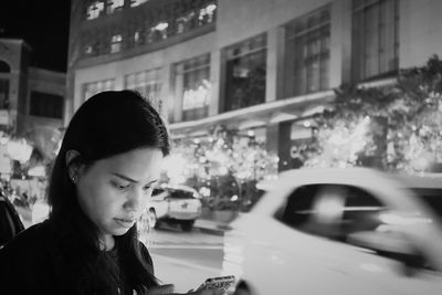 Woman using mobile phone by street in city at night