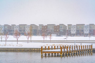 Buildings by river against clear sky during winter