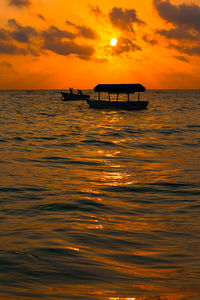 Silhouette boat in sea against orange sky