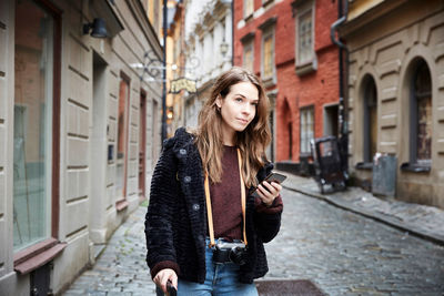 Young woman with mobile phone looking away while standing in alley