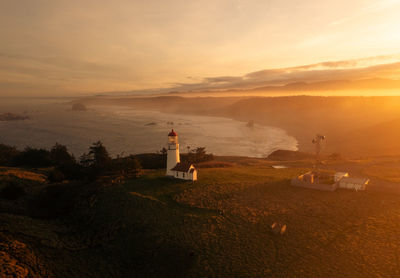 Lighthouse by sea against sky during sunrise