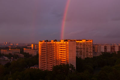 Rainbow over buildings in city against sky at sunset