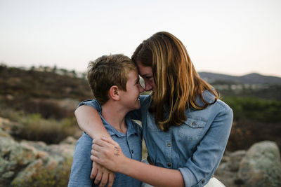 Playful siblings rubbing noses while standing on field during sunset