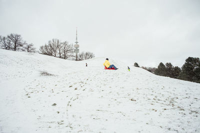 Man sledding on snow covered hill against sky