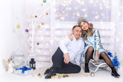 Portrait of happy father with daughter by artificial christmas tree on floor