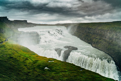 Scenic view of waterfall against cloudy sky