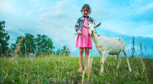 Front view of girl feeding grass to goat