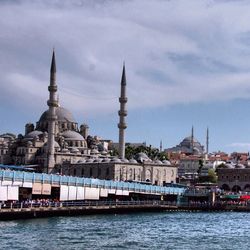 View of city at waterfront against cloudy sky