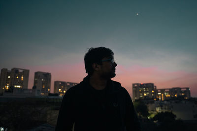 Man standing by illuminated city against sky at sunset