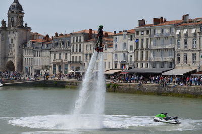 Man flyboarding in sea against building in city