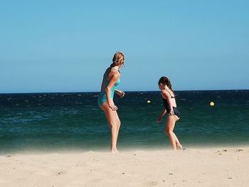 Side view of mother and daughter at beach against clear sky
