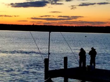 Silhouette men fishing by sea against sky during sunset