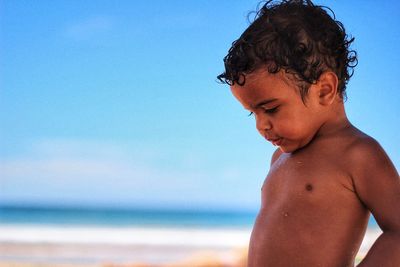 Midsection of shirtless boy at beach against sky