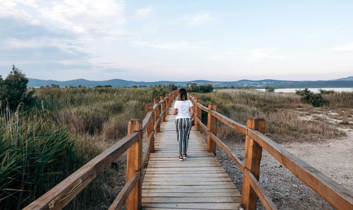 Rear view of young woman on wooden path in nature park.