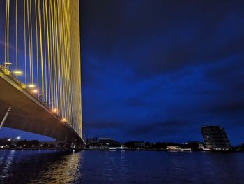 Illuminated bridge over river by buildings against sky at night