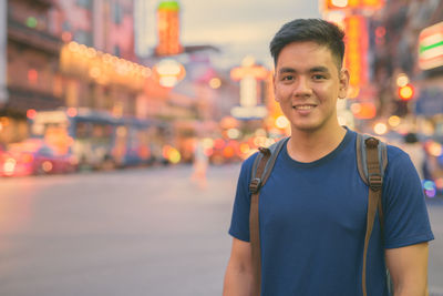 Portrait of smiling young man standing in city at night