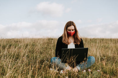 Young woman using laptop while sitting on field