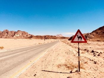 Road sign in desert against clear blue sky