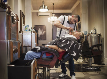 Barber shaving man's beard in shop