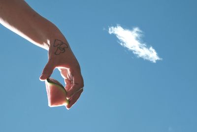 Cropped hand holding watermelon against blue sky