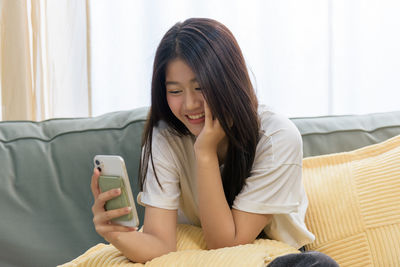 Young woman using phone while lying on sofa at home