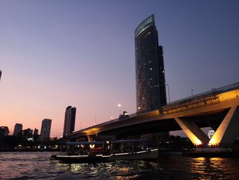 Bridge over river in city against clear sky during sunset