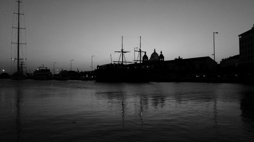 Silhouette of harbor by river against sky