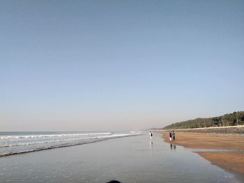 People walking on shore at beach against clear sky