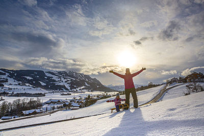 Man with arms outstretched on snowcapped mountain against sky