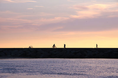 Silhouette people by sea against sky during sunset