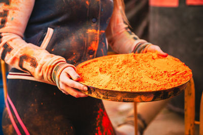 Midsection of man holding orange powder paint in tray during holi