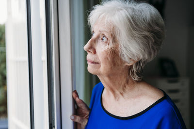 Thoughtful senior woman looking through window at home
