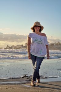 Full length of woman standing at beach against sky during sunset