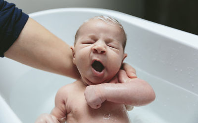 Cropped hands of mother bathing son in bathtub at bathroom