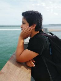 Young man sitting on sea shore against sky