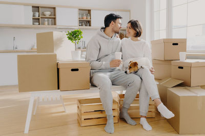 Couple with dog talking while sitting amidst boxes in new home