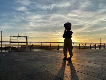 Full length of silhouette woman standing on railing against sky