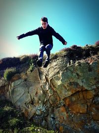 Full length of boy jumping on rock against sky