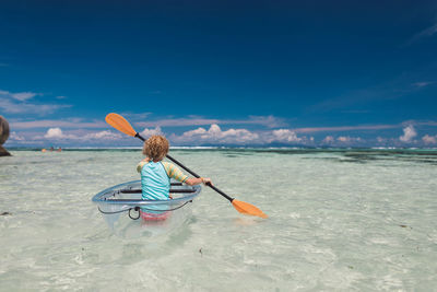 Rear view of woman rowing on sea against sky